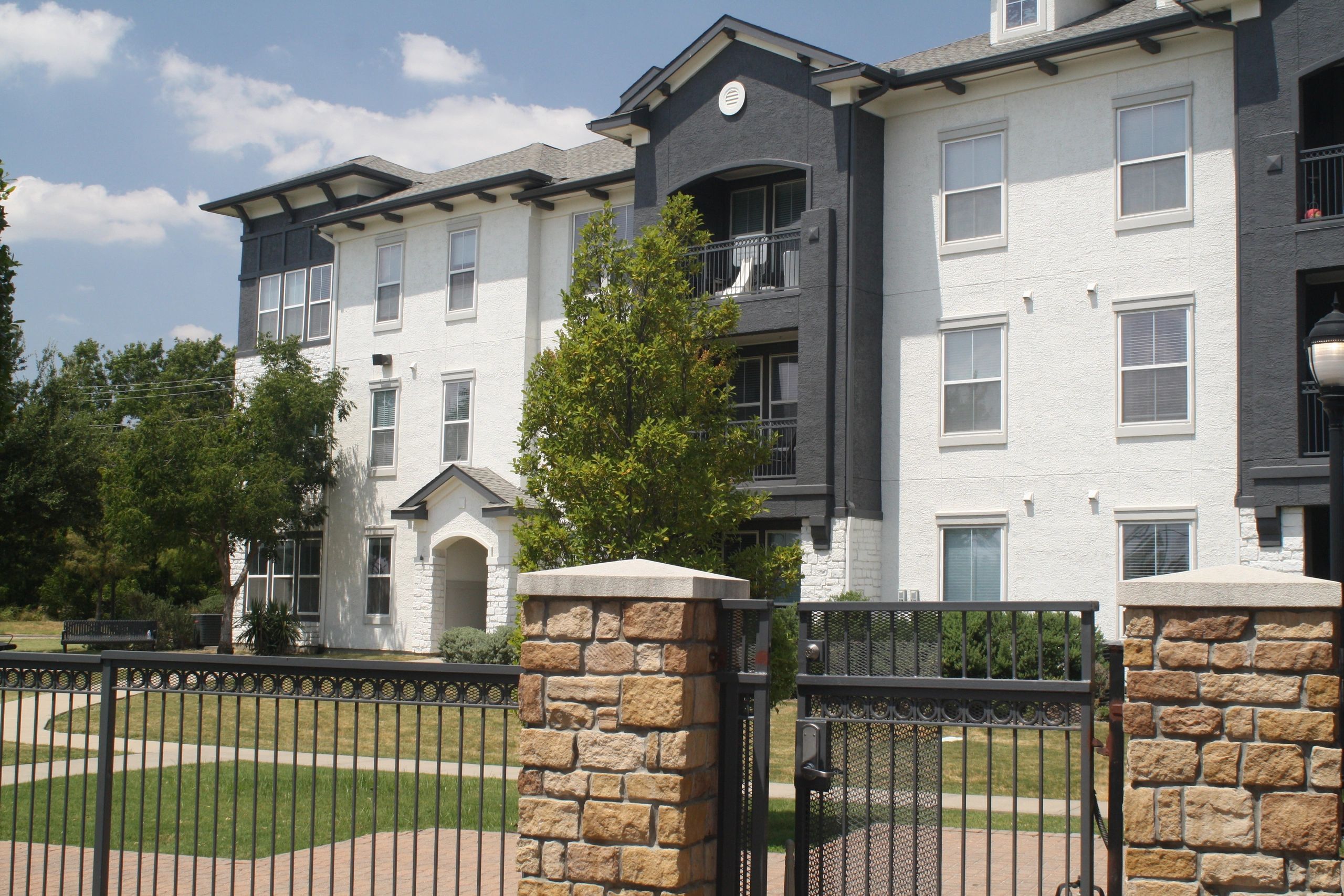 Multifamily building exterior with a stone gate pillar and iron fence
